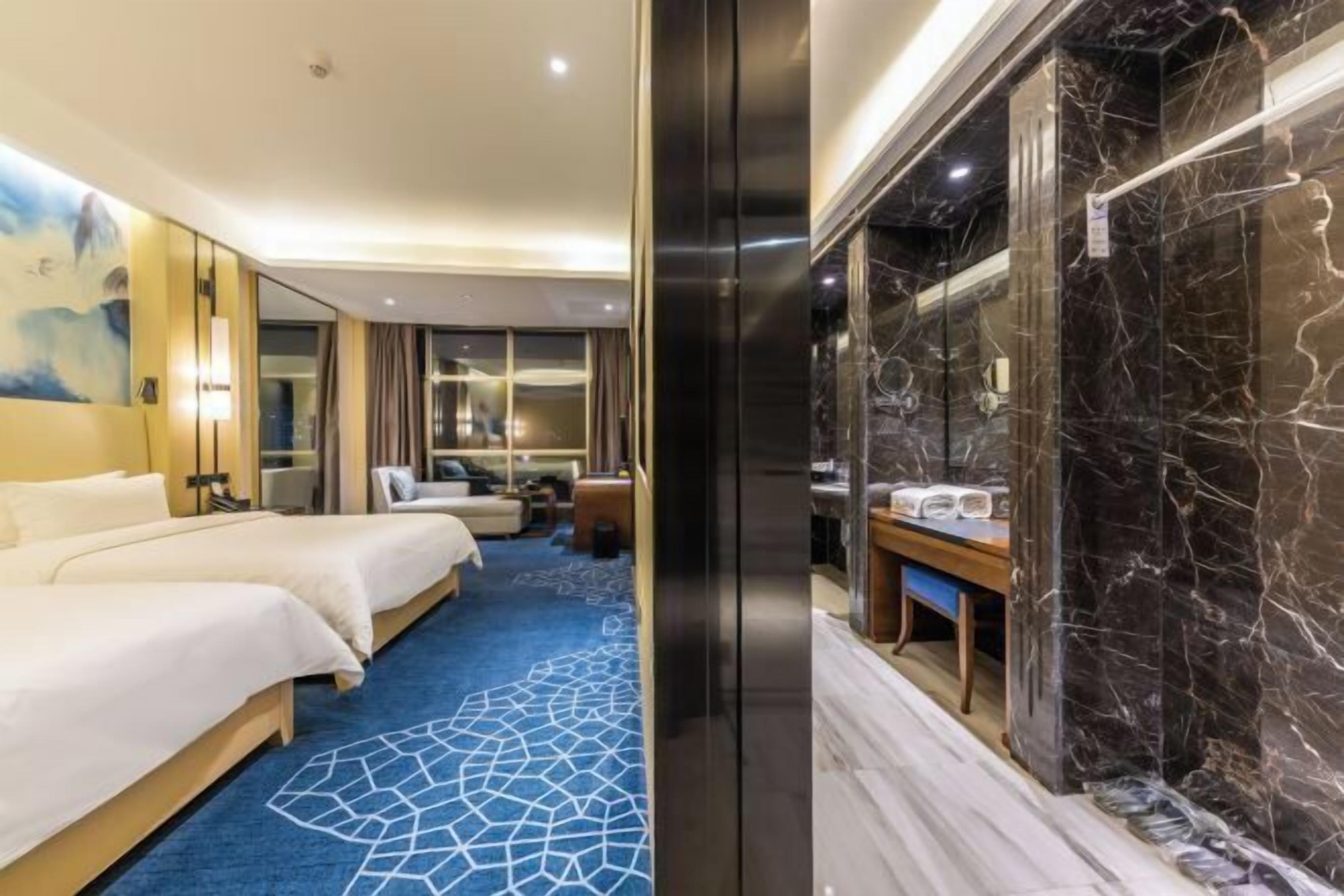 A hotel room with a large bed, a desk, a bathroom with a marble wall, and a blue carpet.