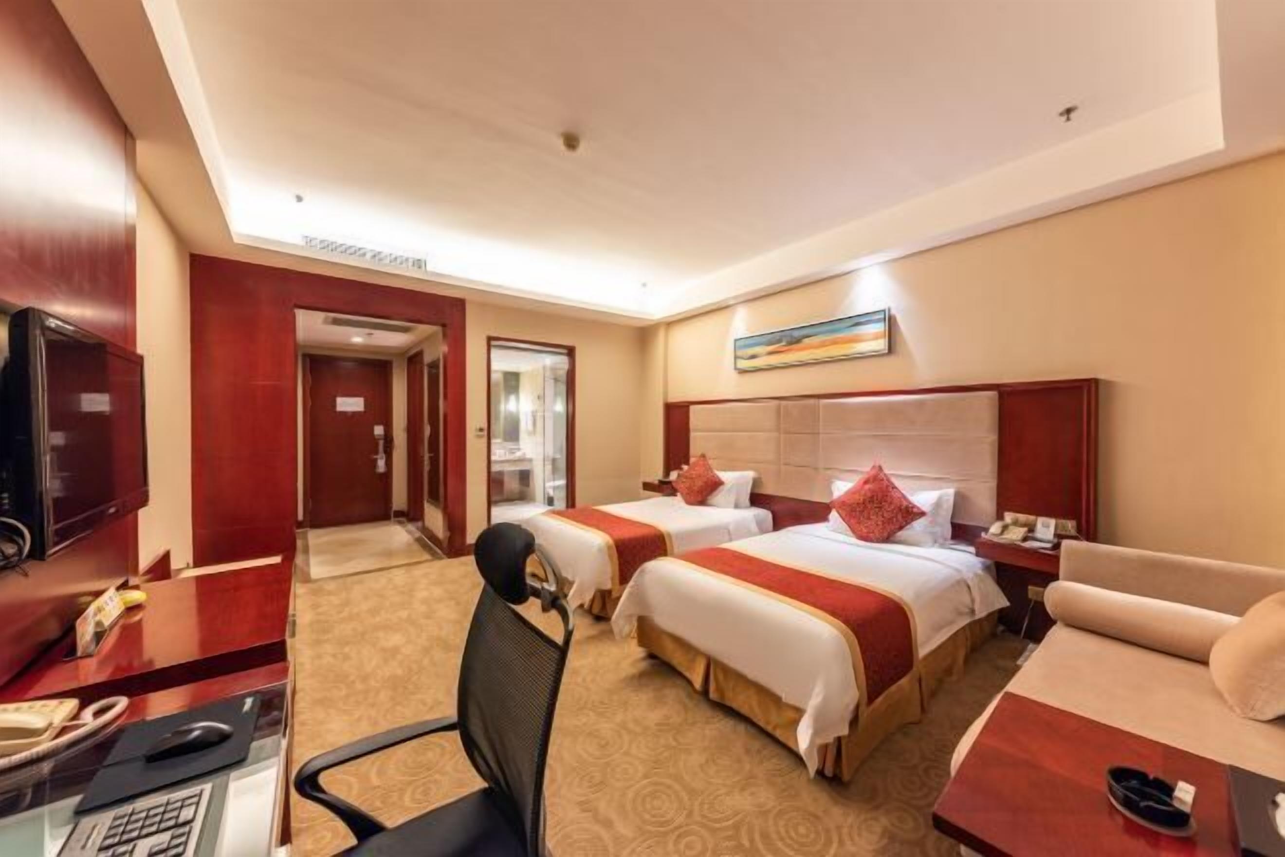 Una habitación de hotel con dos camas, un escritorio con computadora y teléfono, una televisión y un sofá.