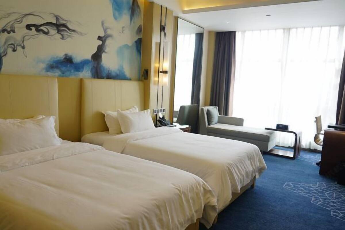 A hotel room with two beds, a sofa, a small table, and a large window with curtains.