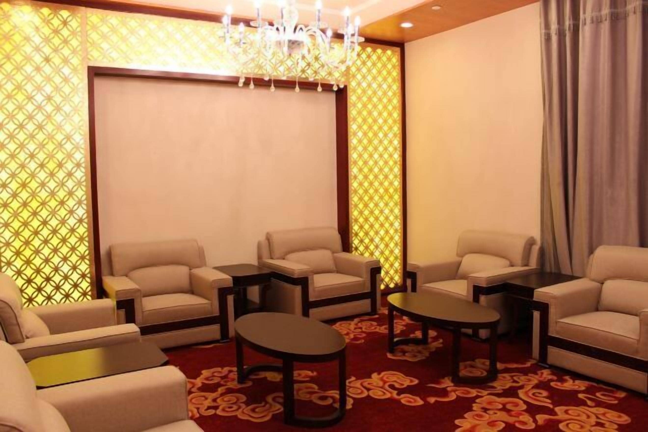 A room with four beige armchairs, two small tables, a chandelier, and patterned curtains.