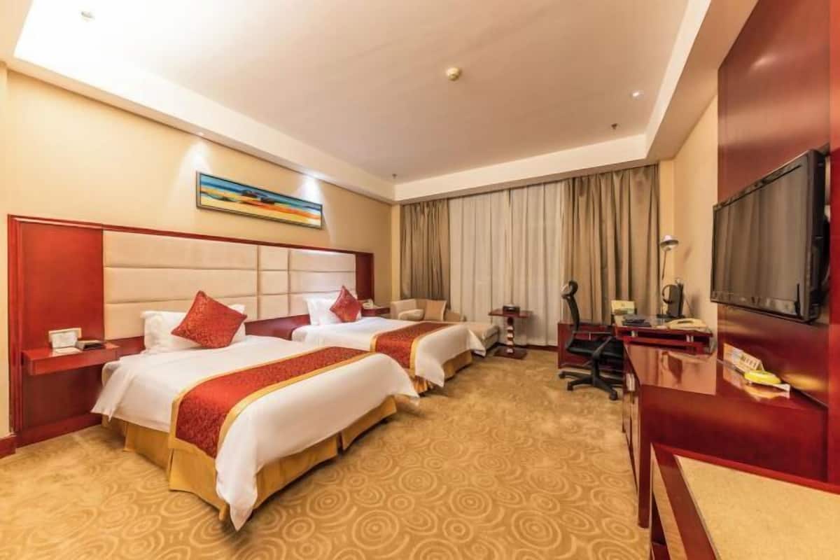 A hotel room with two beds, a desk, a TV, and a painting on the wall.