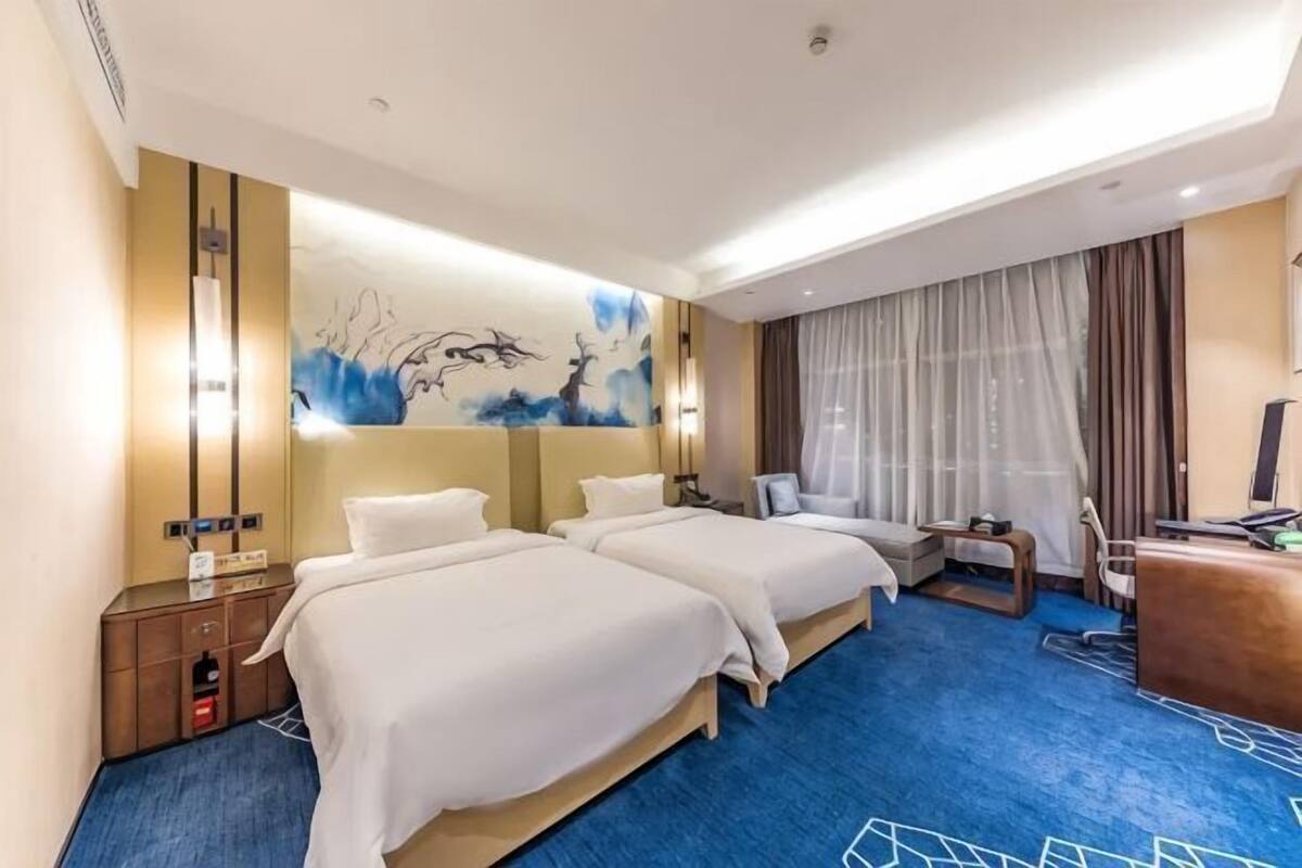 A hotel room with two beds, a desk, a chair, a TV, and a painting on the wall.