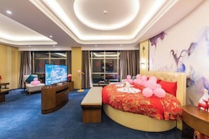 Habitación de hotel con una cama grande, un televisor y vistas a la ciudad desde las ventanas.