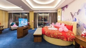 A hotel room with a large bed, a television, a desk, and a view of the city through the window. - Longtan Hotel (Wuxue)