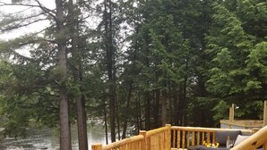 A wooden deck with a railing overlooking a river, surrounded by tall trees. - Adirondack/Oswegatchie Riverfront Cabin (Harrisville)
