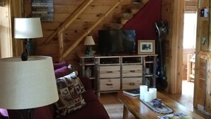 A cozy cabin interior with a wooden ceiling, a sofa, a dining table, and a television. - Adirondack/Oswegatchie Riverfront Cabin (Harrisville)