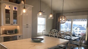 Una cocina con isla de mármol, gabinetes blancos e iluminación colgante.