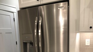 Un refrigerador de acero inoxidable con dispensador de agua, armarios blancos y piso de madera.