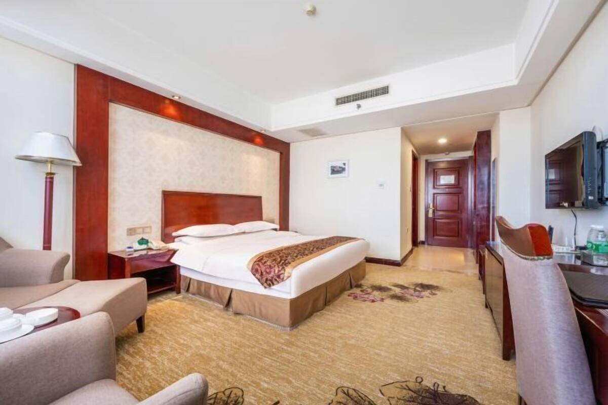 Una habitación de hotel con cama, escritorio, silla, lámpara y televisión.