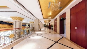 Corredor de hotel com piso de mármore, uma porta vermelha e um candelabro.