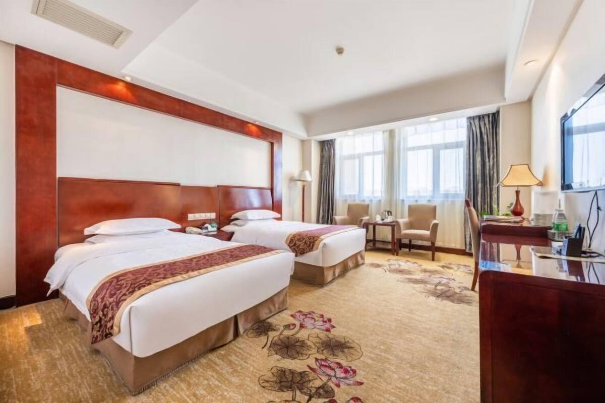 Habitación de hotel con dos camas, un escritorio, una silla y un ventanal grande.