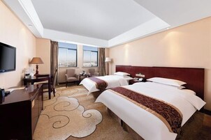A hotel room with two beds, a desk, a chair, a TV, and a view of the city.