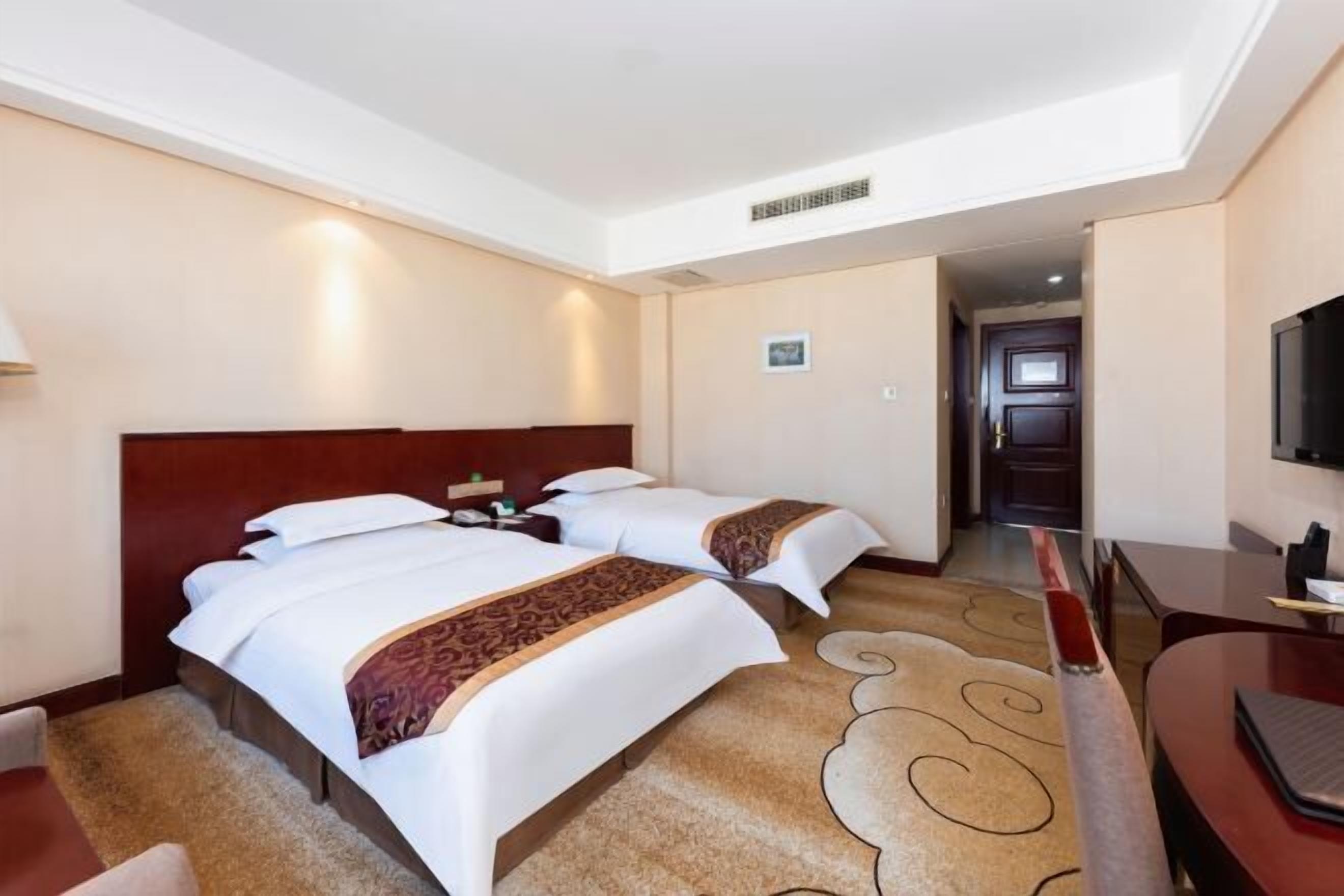 Habitación de hotel con dos camas, televisión, escritorio y piso alfombrado.