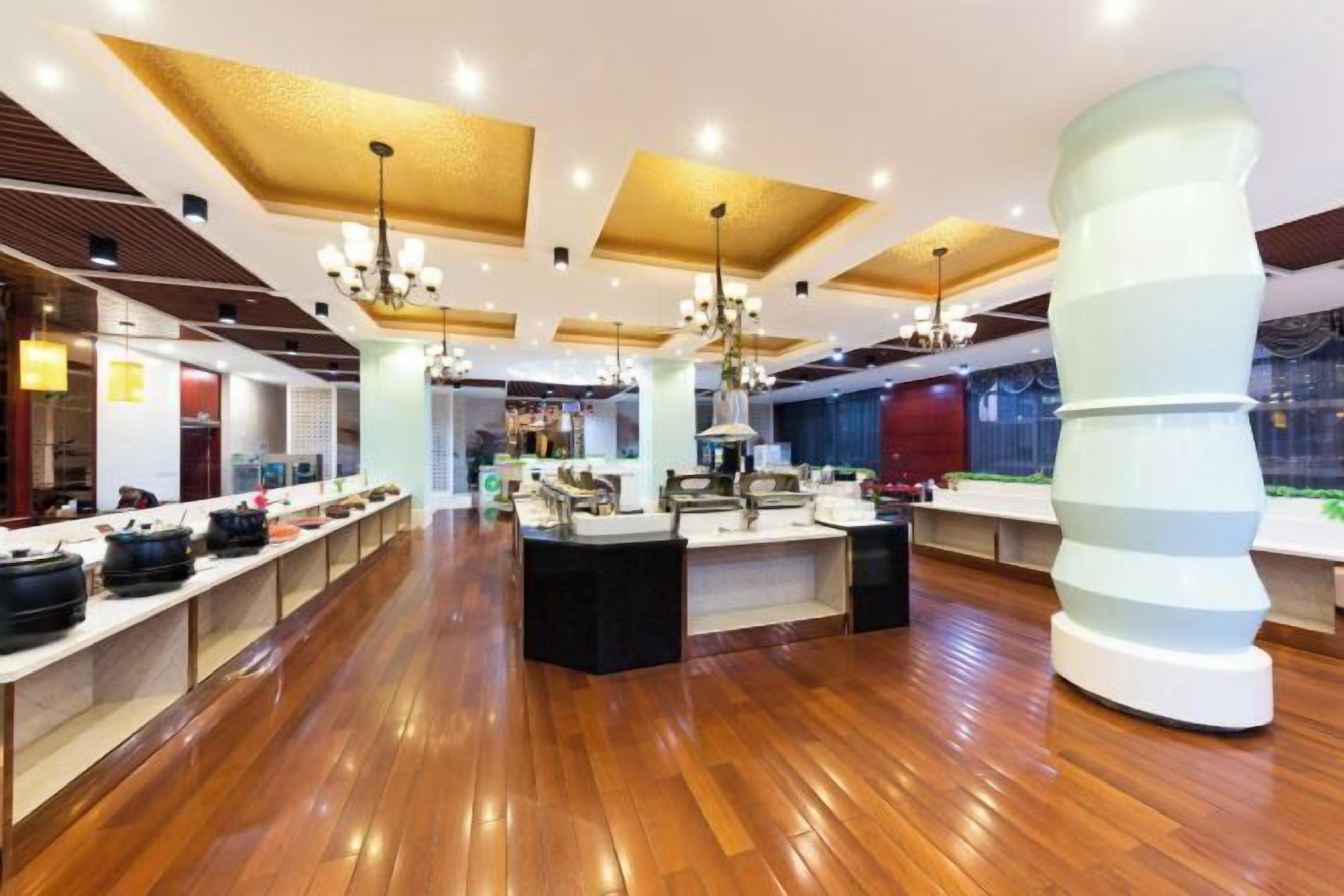 A modern hotel lobby with wooden flooring, a central reception desk, and a large decorative sculpture.