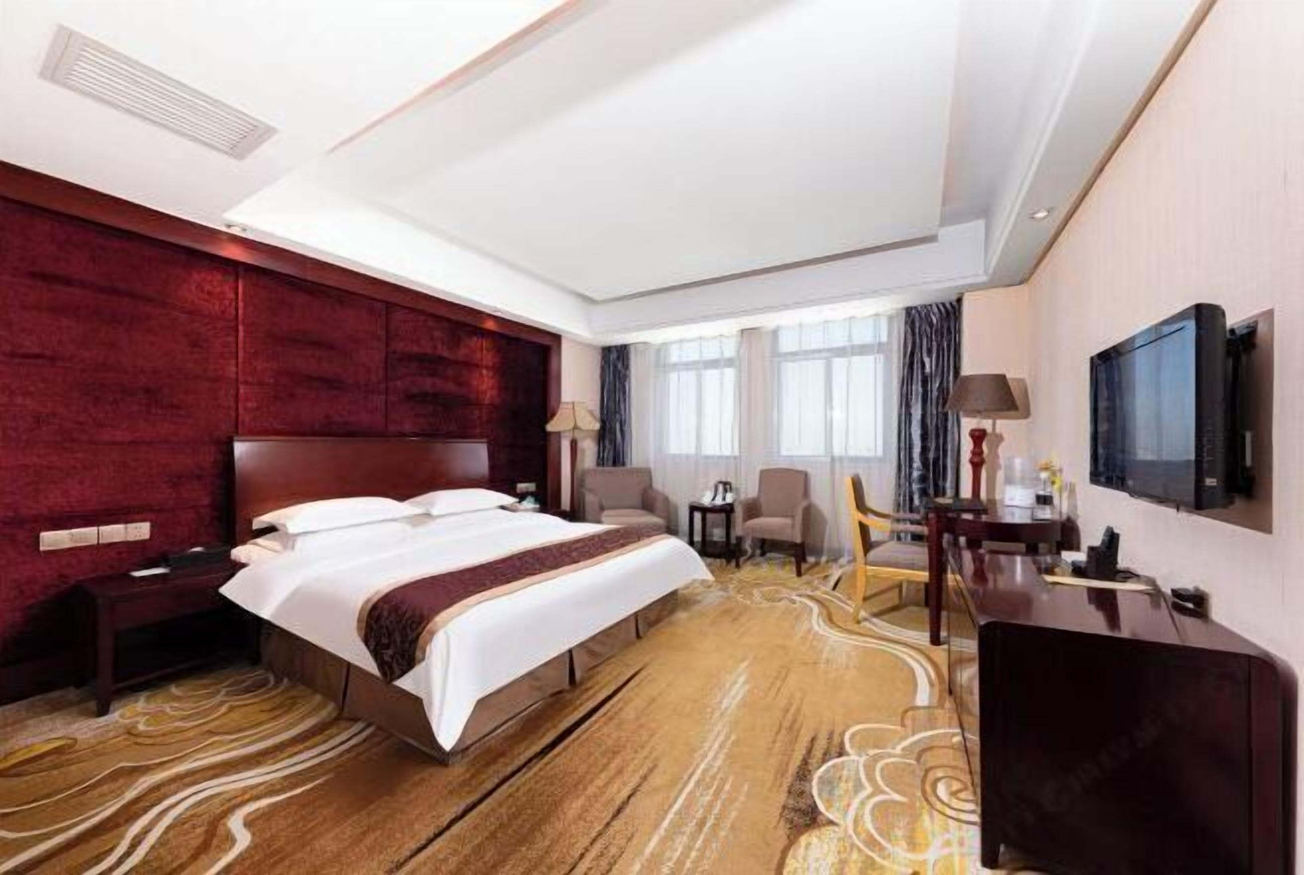 A hotel room with a large bed, a desk, a chair, a TV, and a window.