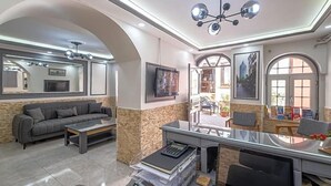 A modern living room with a sofa, a coffee table, a desk with a computer, and a television. There are framed pictures on the walls and a chandelier. - Sur Hotel Sultanahmet (Istanbul)