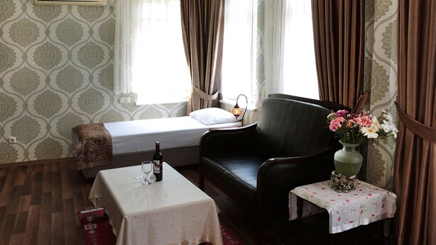 A hotel room with a bed, a chair, a small table with a bottle and glasses, and a vase with flowers. - Sur Hotel Sultanahmet (Istanbul)