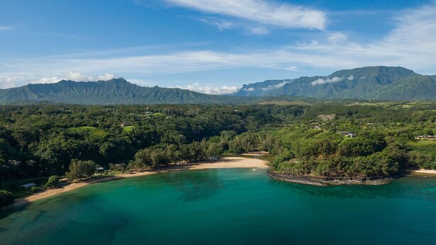 Paisaje costero con una playa, aguas turquesas cristalinas y montañas al fondo.