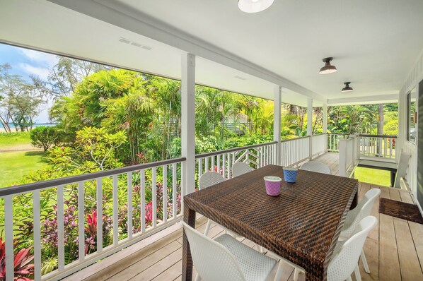 A covered outdoor area with a table and chairs, surrounded by white railings and lush greenery.