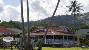 Una cafetería con porche y luces colgantes, rodeada de palmeras y un paisaje exuberante.