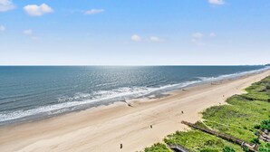 Ein weiter Sandstrand mit einem hölzernen Promenadenweg zum Wasser, bewölkter Himmel und sanften Wellen.