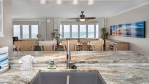 A kitchen with a large island, a ceiling fan, and a view of the ocean through large windows.