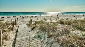 A wooden boardwalk leading to beach chairs and umbrellas, with a sandy beach and ocean in the background.