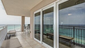 A balcony with a view of the ocean, a table with chairs, and a bench.