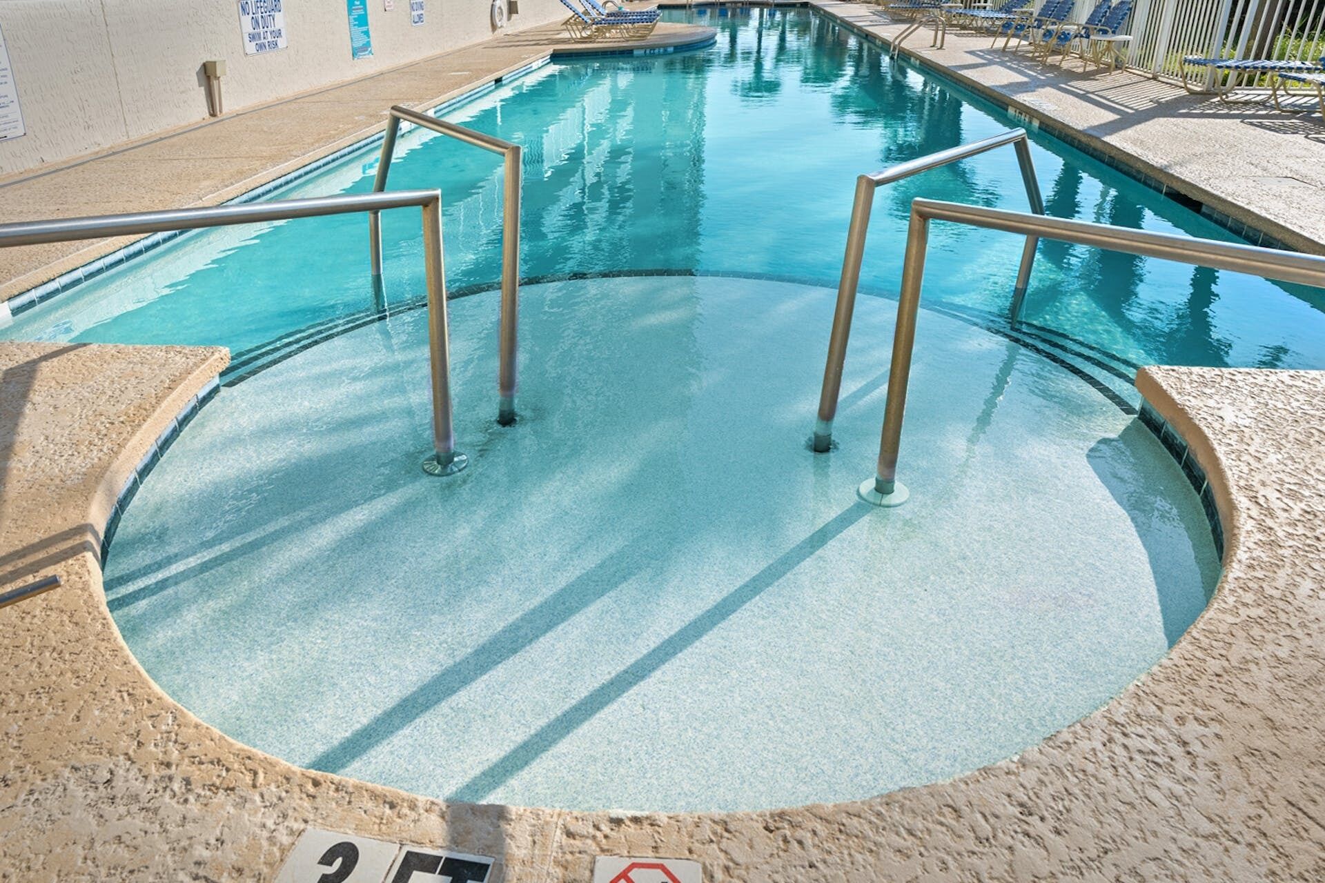 A swimming pool with metal railings and a no lifeguard sign.