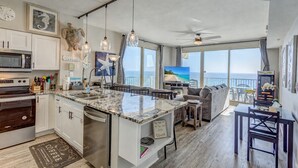 Eine moderne Küche mit einer großen Kochinsel, ein Essbereich mit Blick und ein Wohnzimmer mit großem Fernseher.