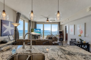 A spacious living area with a large window overlooking the ocean, a kitchen with granite countertops, and a ceiling fan.