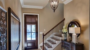 A hallway with a wooden staircase, a dark console table with a lamp, and a decorative mirror. - Close to Golf Course, Pool, Beach, Baytowne!  Large home (2153 Sq Ft)- Peace of Heaven at Villa Lago (Miramar Beach)