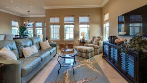A spacious living room with a leather sofa, a round coffee table, and a TV on a cabinet. - Close to Golf Course, Pool, Beach, Baytowne!  Large home (2153 Sq Ft)- Peace of Heaven at Villa Lago (Miramar Beach)