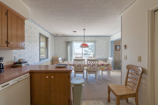 A kitchen with wooden cabinets, a dishwasher, and a dining area with a table and chairs.
