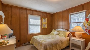 Ein Schlafzimmer mit Holzwandverkleidung, einem Bett mit floralem Bettzeug, zwei Nachttischlampen und einem Nachttisch mit Muscheldekoration.