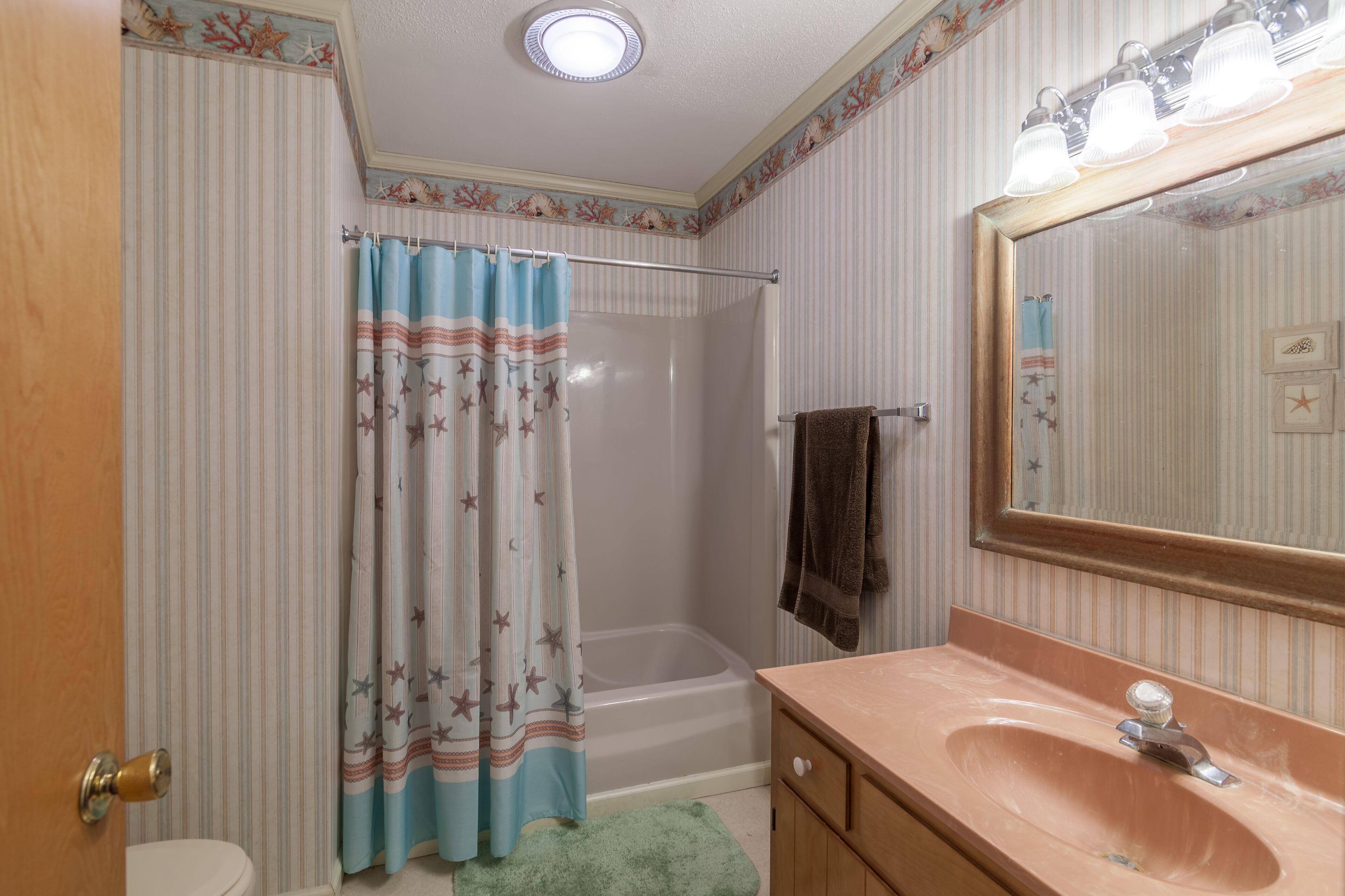 A bathroom with a striped wall, a bathtub, a sink, and a mirror with lights.