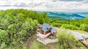 A large, two-story house with a spacious deck and a covered patio, surrounded by lush greenery and hills in the background. - Near Asheville, near the stars, nearly perfect!  Almost Heaven.  3000 ft. (Old Fort)