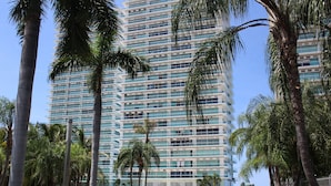 Ein modernes Hochhaus-Hotel mit mehreren Etagen, umgeben von Palmen und blauem Himmel.