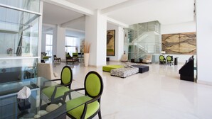Eine geräumige Lobby mit einem Glastisch, grünen Stühlen, einer Couch und einer Treppe.