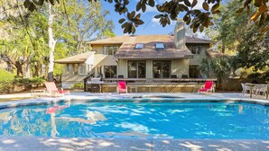 Una propiedad residencial con piscina, un patio cubierto y una casa grande con muchas ventanas.