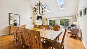 Un comedor amplio con una mesa y sillas de madera, un candelabro y vistas al exterior a través de amplios ventanales.