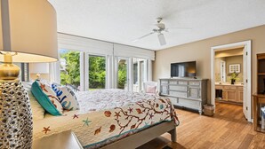 Un dormitorio con cama, ventilador de techo, cómoda, televisor y vistas al exterior.