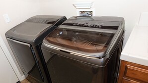 Un appareil compact combinant lave-linge et sèche-linge, installé dans un petit espace cuisine, avec un plan de travail blanc et des placards en bois.