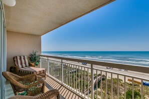 Ein Balkon mit Korbmöbeln, Blick auf den Strand und einem klaren Himmel.