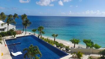 A pool with a view of the ocean, surrounded by palm trees and a beach.