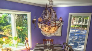 Comedor con una gran mesa de madera dispuesta para seis personas, rodeada de sillas, y un candelabro decorativo colgando en lo alto.