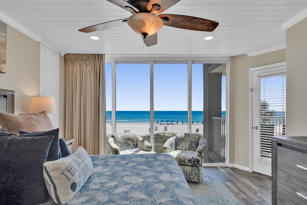 Un balcon avec vue sur la plage, un ventilateur de plafond et un canapé recouvert d’un tissu à motifs.