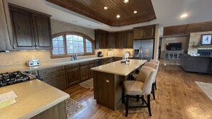 A modern kitchen with wooden cabinets, a central island, and a dining area with chairs.