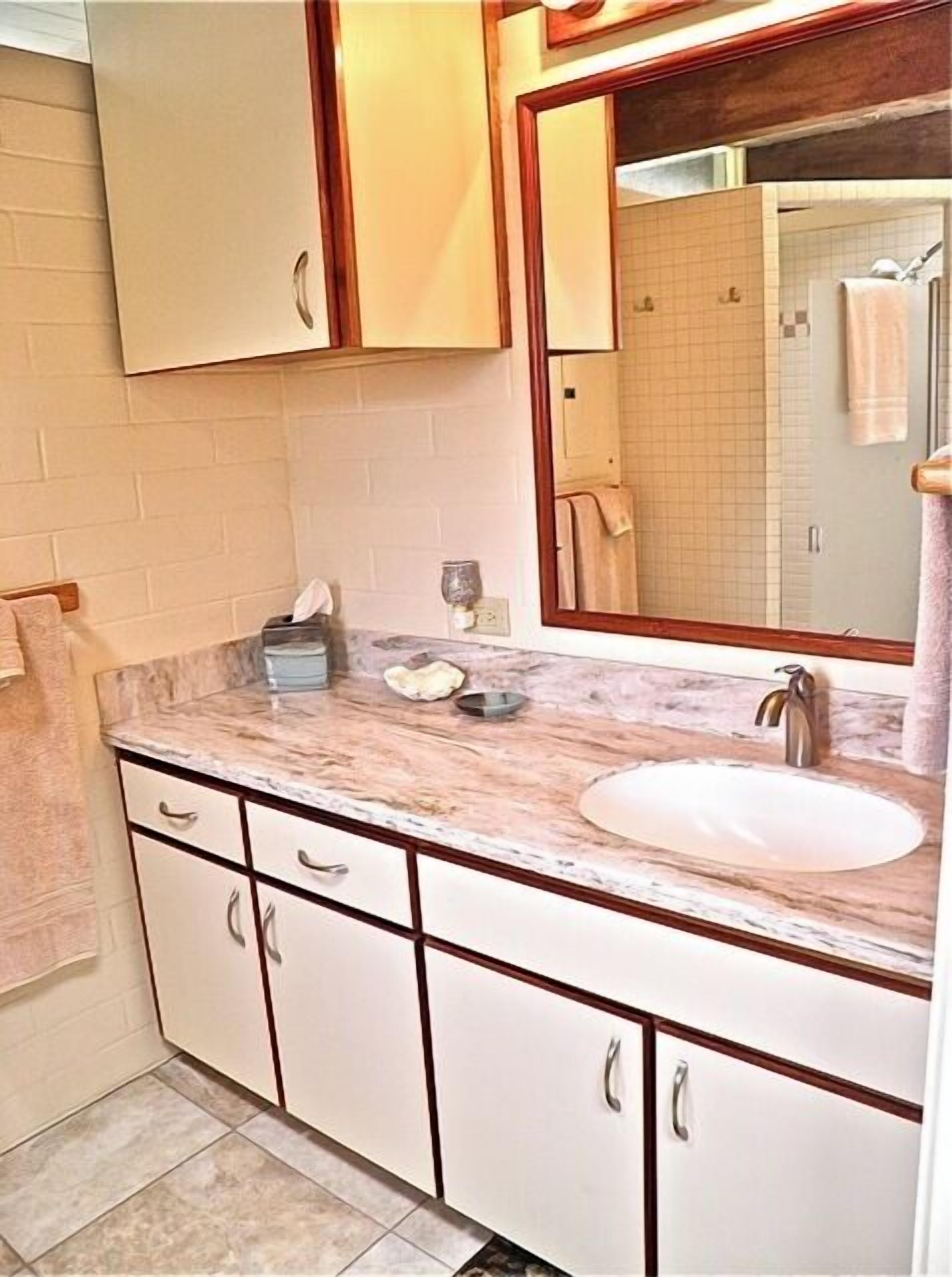 A bathroom with a marble countertop, a sink, and a mirror. There are cabinets and a towel rack visible.