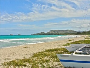 A beach with a clear sky, calm sea, and distant mountains.
